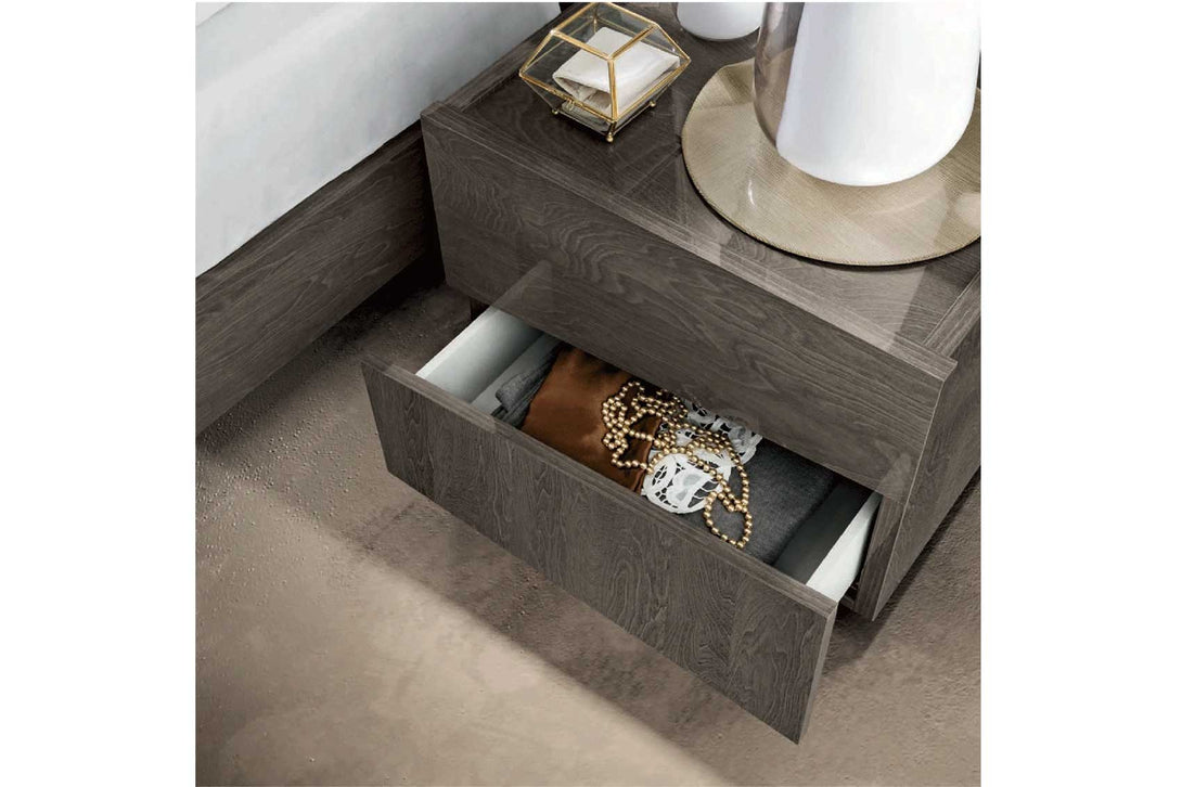 Wooden nightstand with open drawer containing jewelry, on a neutral background