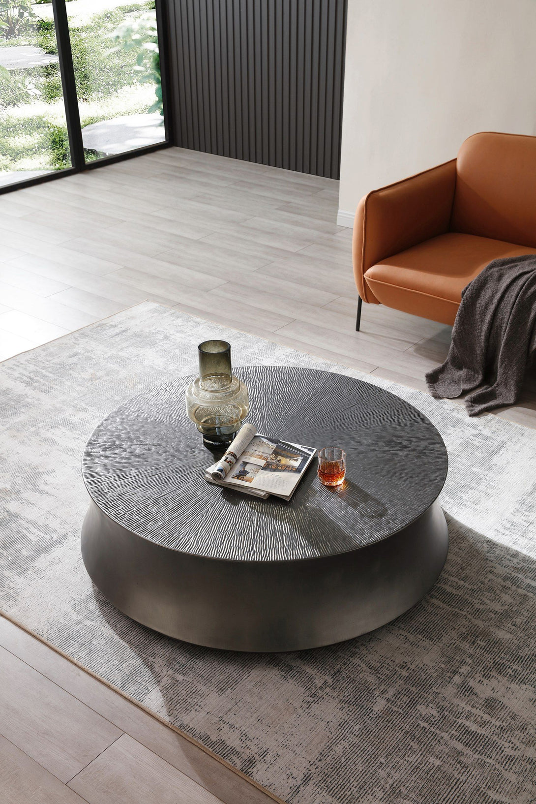Round coffee table in a modern living room with a brown sofa and large windows.