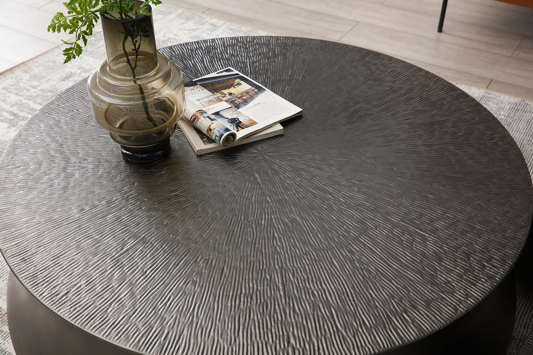 Round dark gray table with a vase and magazine on a light wooden floor.