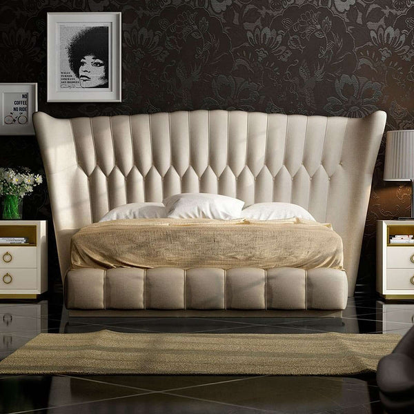 Beige tufted bed in a bedroom setting with dark floral wallpaper.